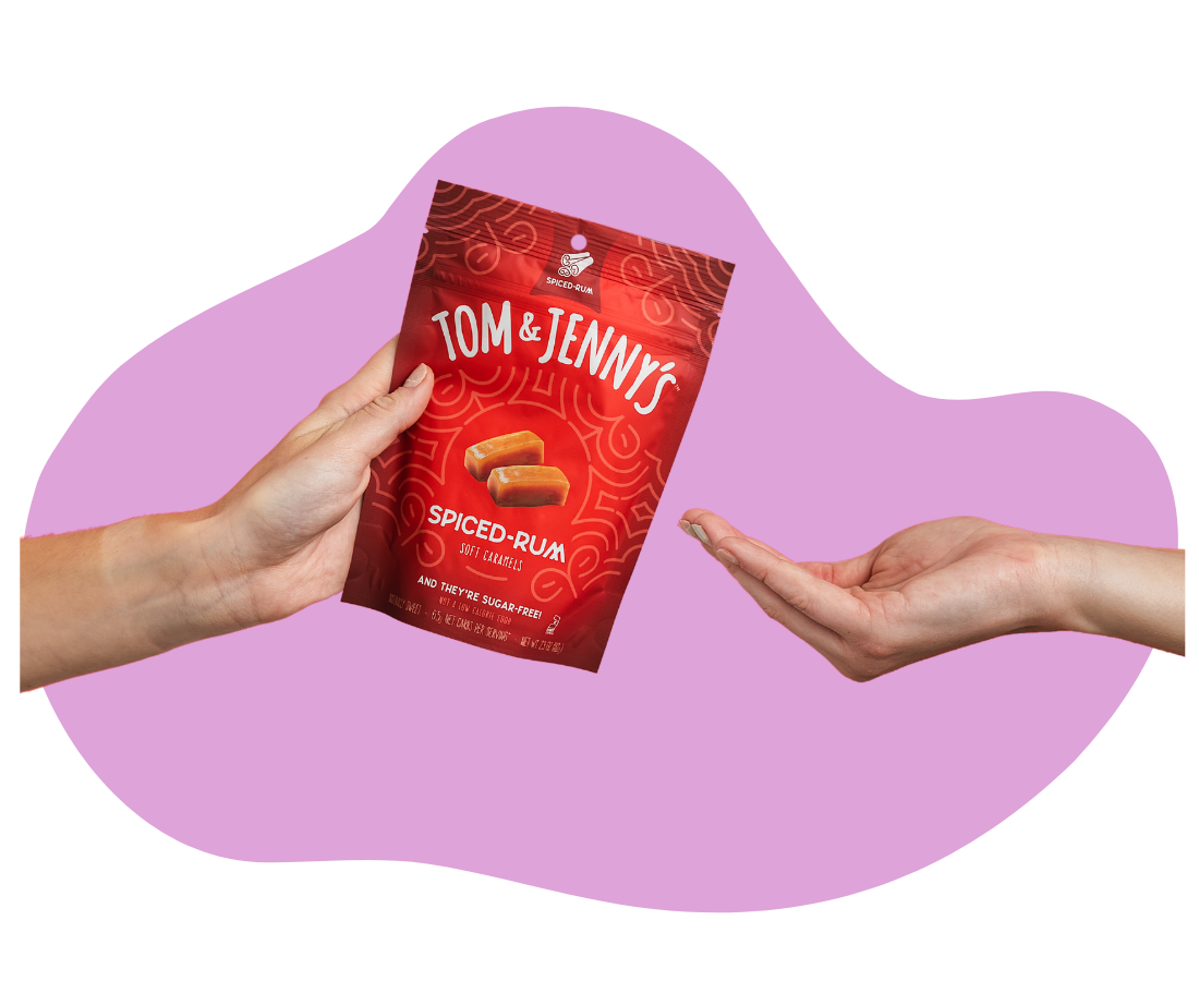 Image of a hand holding a bag of Spiced Rum caramels and another cupped hand waiting to receive them