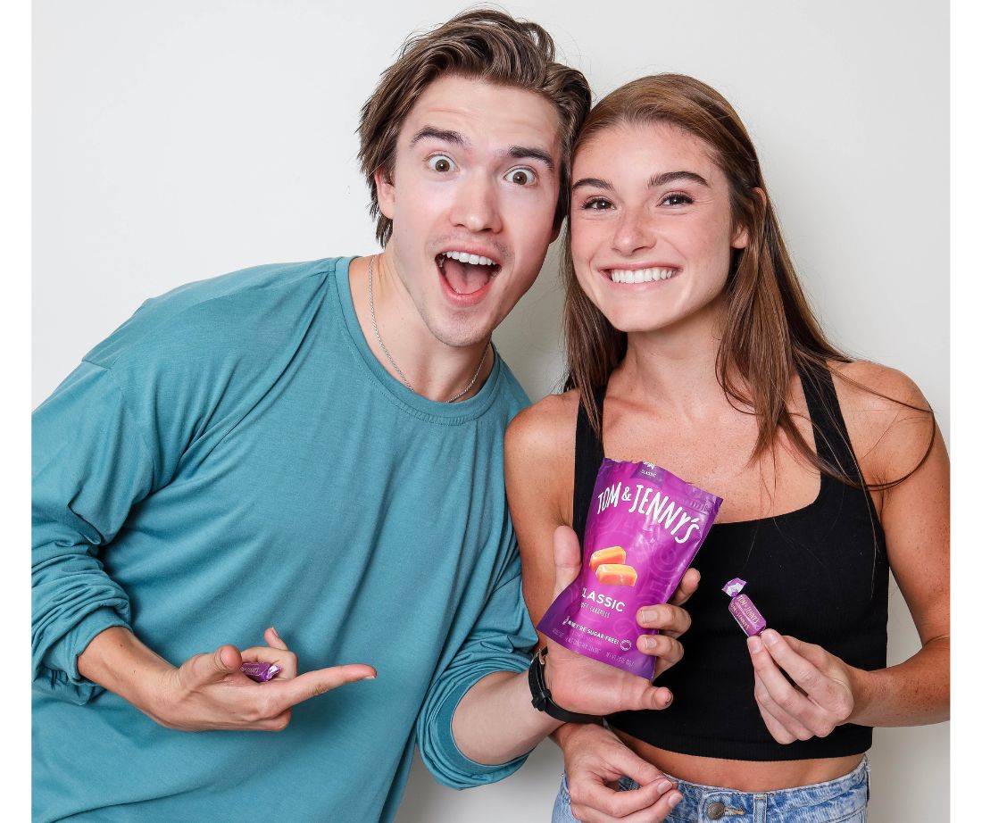Image showing a young man and woman smiling with expressions of excitement as they hold a bag of classic caramel and some pieces of classic caramels.