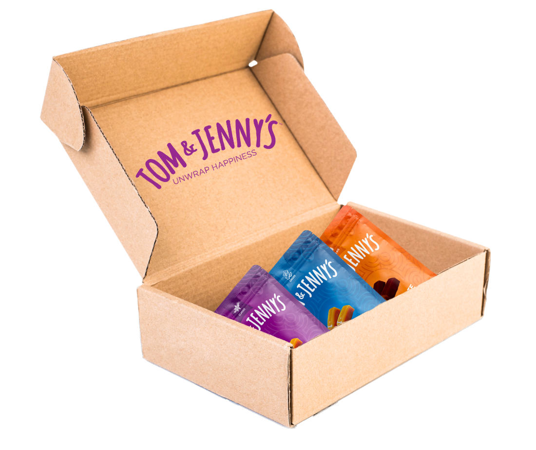 Image of a cardboard box containing a Classic, Ginger, and Chocolate bag of Tom & Jenny's caramels.