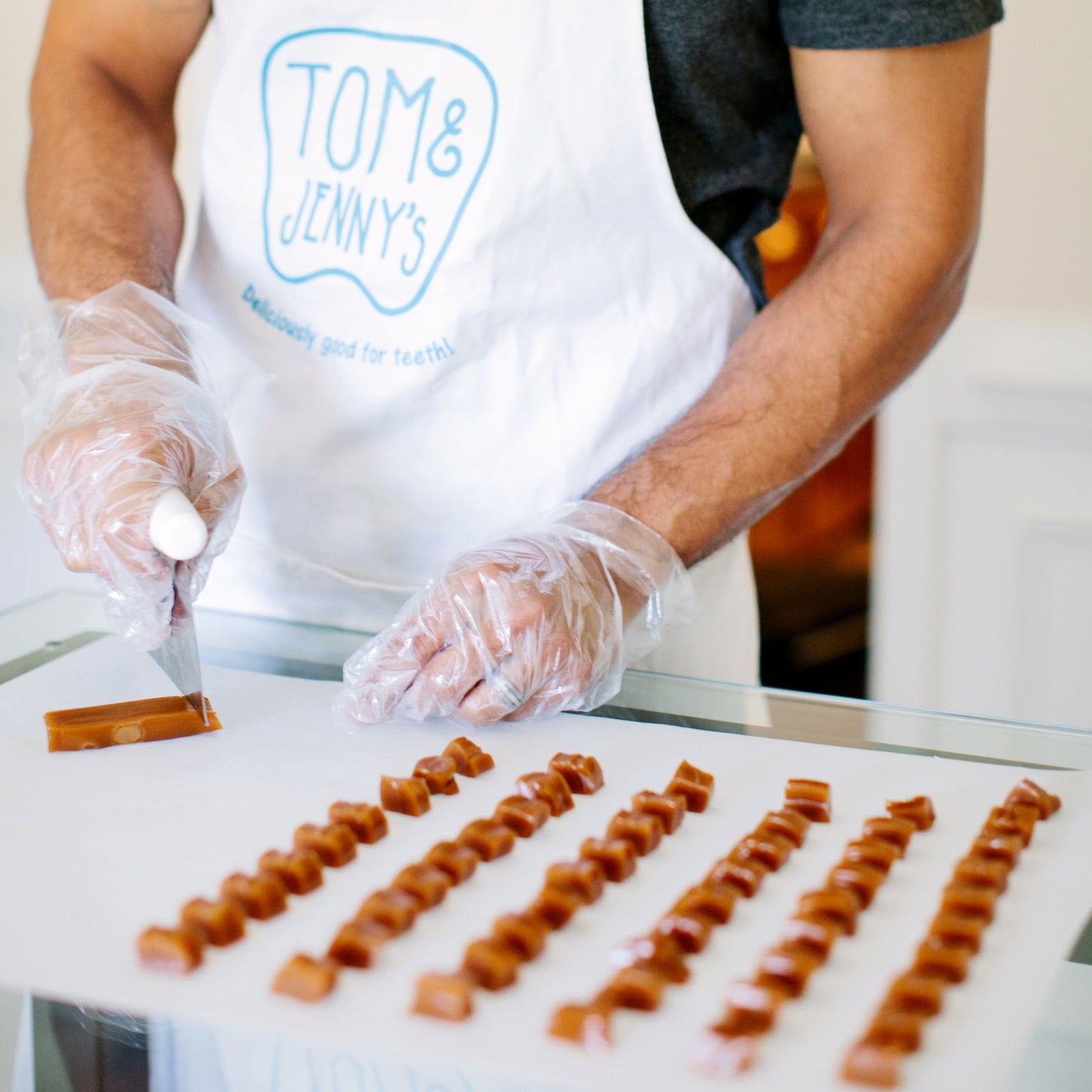 Image of Tom cutting a large bar of freshly cooled caramel into individual pieces on a cutting sheet