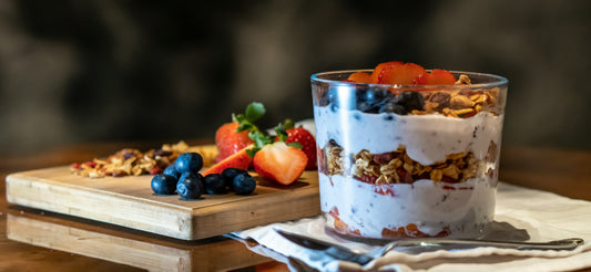 A layered greek yogurt parfait in an elegant glass, showing alternating layers of greek yogurt, with granola and berries in between layers and on top