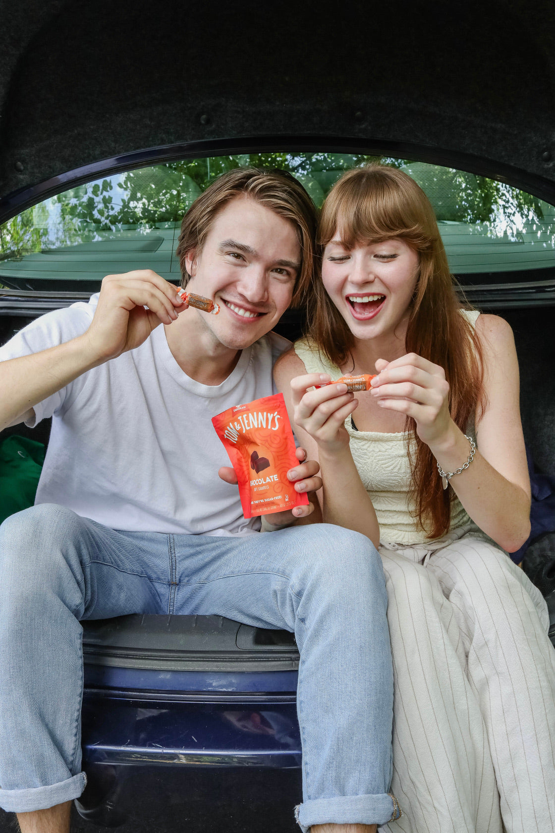 Image of man and woman sitting on back of car smiling with Chocolate Tom & Jenny's in hand