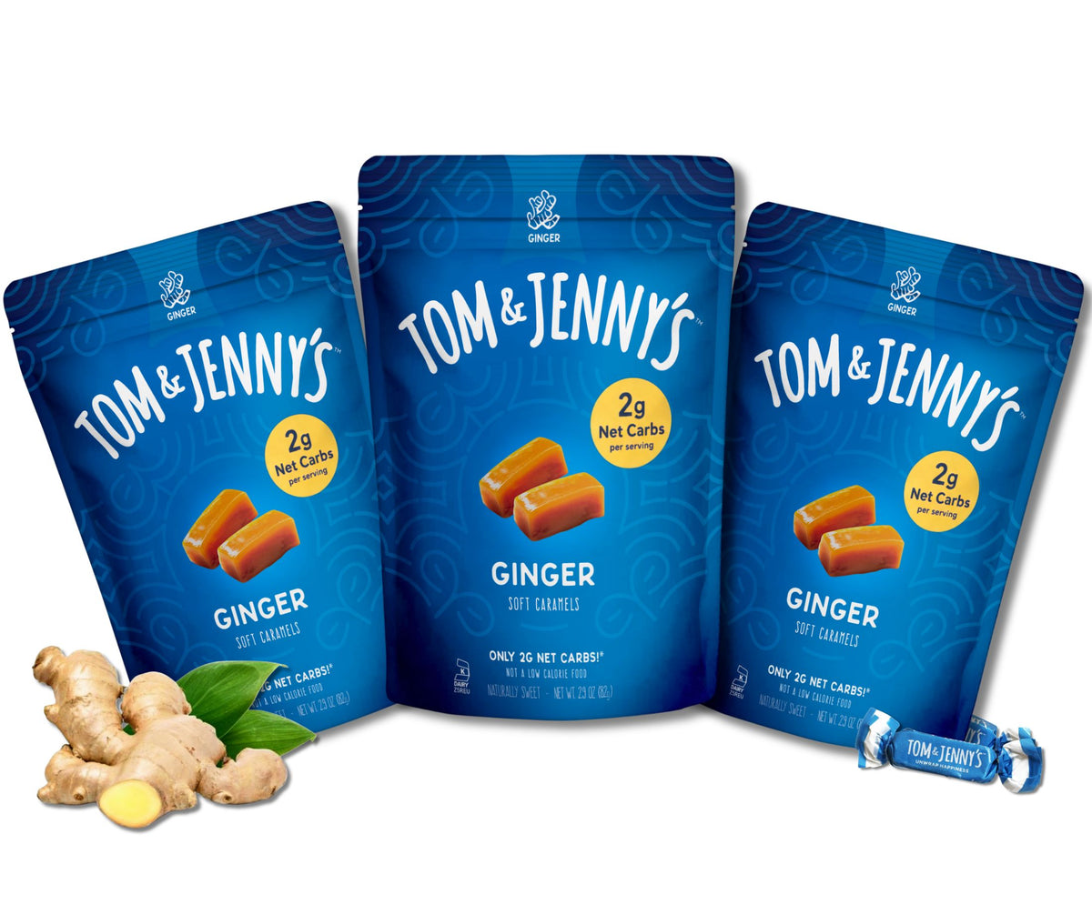 Three blue Tom & Jenny's Ginger Soft Caramels pouches arranged together on a white background, with ginger root pieces and green leaves at the lower left and a wrapped candy at the lower right.