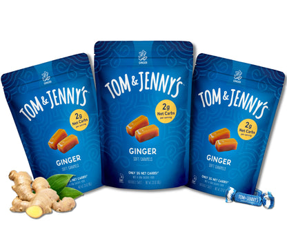 Three blue Tom & Jenny's Ginger Soft Caramels pouches arranged together on a white background, with ginger root pieces and green leaves at the lower left and a wrapped candy at the lower right.