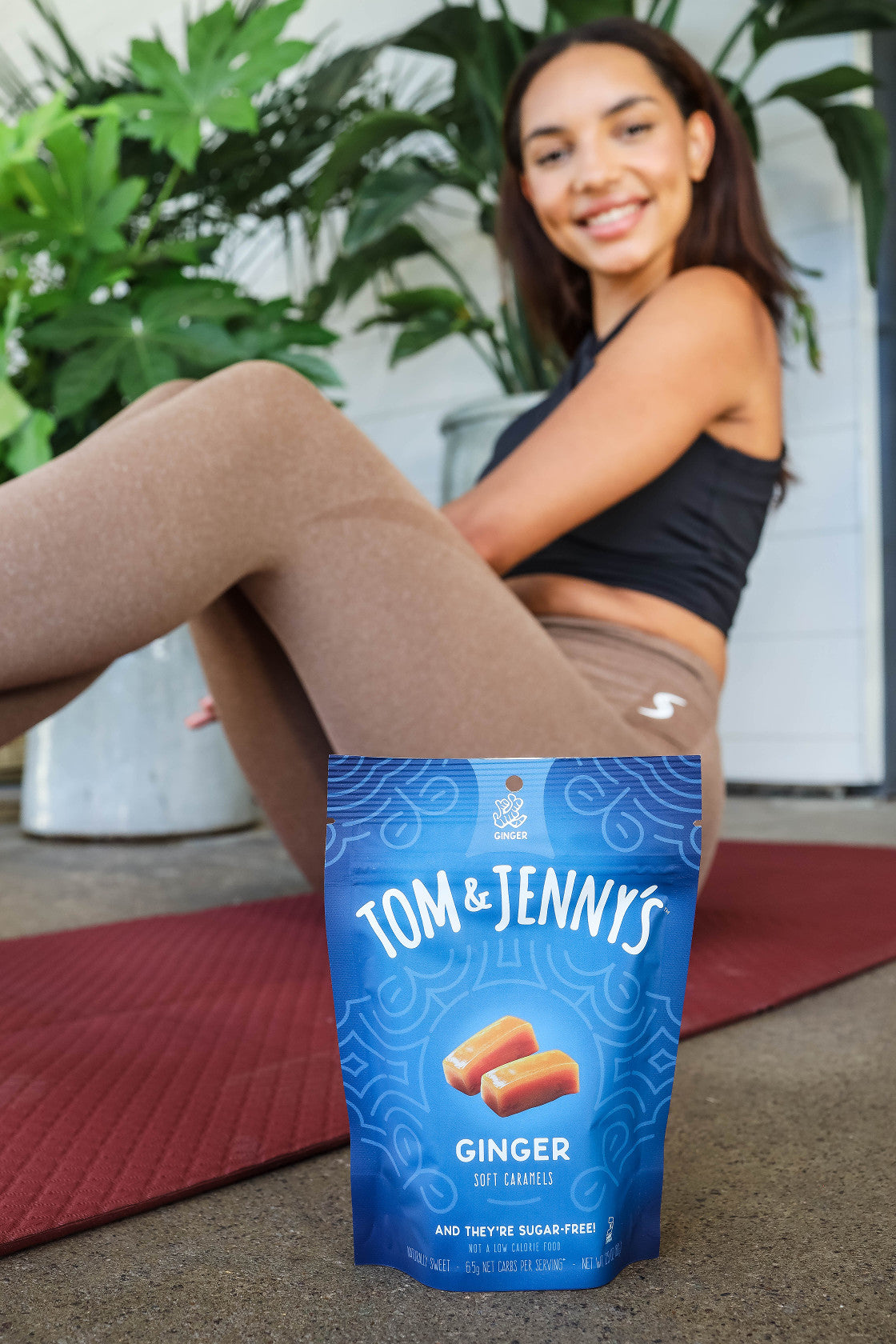 Image of woman sitting on a yoga mat with a bag of Ginger Tom & Jenny's caramels in front of her