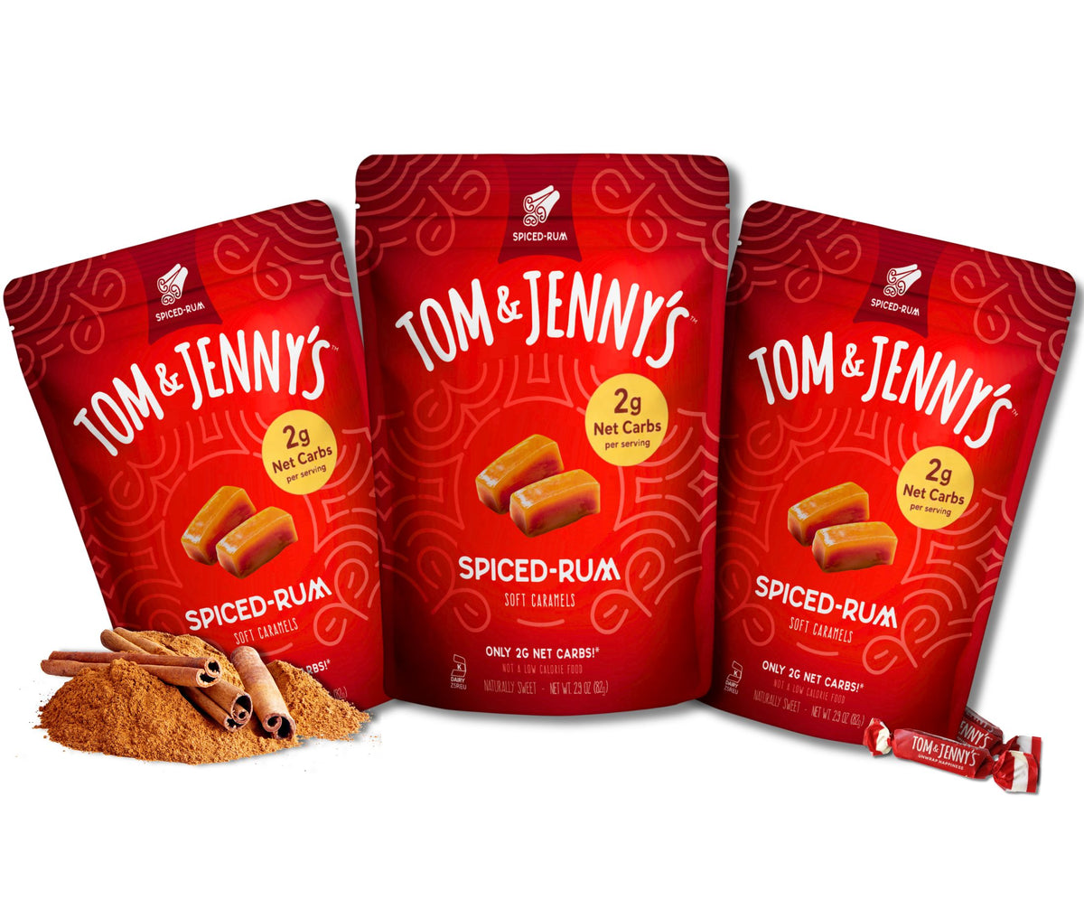 Three red Tom & Jenny's Spiced-Rum soft caramel pouches arranged on a white background, with cinnamon sticks  beside them.