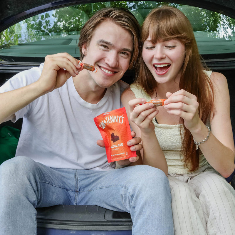A picture of two people sitting in the open trunk of a car holding up chocolate Tom & Jenny's and smiling